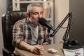 A gray-haired man with a beard smokes while recording a podcast. A man in a plaid shirt sits at a table with a cigarette Royalty Free Stock Photo