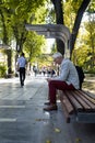 Gray-haired man with smartphone in his hands is sitting on wooden bench in city park on warm autumn day. Outdoor recreation. Royalty Free Stock Photo