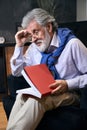 Gray-haired old male sits in cozy armchair with a book Royalty Free Stock Photo