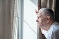Gray-haired old man, forced to remain in quarantine due to the covid-19 coronavirus, looks out the window with a disconsolate Royalty Free Stock Photo