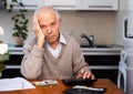 Gray haired old man sitting at table and counting coins and money