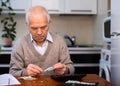 Gray haired old man sitting at table and counting coins and money