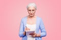 Gray haired old serious business woman wearing glasses, writing plans strategy in paper note book with pen. Isolated Royalty Free Stock Photo