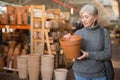 Aged woman selecting decorative earthenware pot in shop