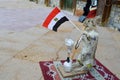 The gray hare stands on the rug holding the Egyptian flag in its paws and smoking a hookah, a scarecrow