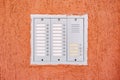 A gray intercom on an orange rough wall.