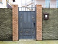 A gray iron gate with a forged pattern in a fence with decorative brick-like tiles and a mailbox on it Royalty Free Stock Photo