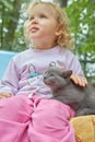 A gray kitten sits on a child's lap. The child is out of focus. Focus on the cat. Royalty Free Stock Photo