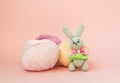 Gray knitted hare stands on the background of multi-colored balls of yarn on a pink background. There is a place for text