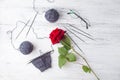 Gray knitting wool, half of handmade sock on needles, black glasses and single red rose on wooden white background. Royalty Free Stock Photo