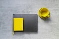 The gray laptop the yellow notebook and cup on a grey concrete background