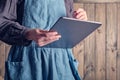 A gray large tablet in female hands in a harmonious cotton dress and a linen emerald apron.