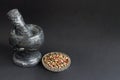 Gray marble mortar and hummer for spices and plate with a mixture of dry peppers on a black background