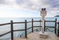 Gray metal binocular stands on a raised platform overlooking the sea