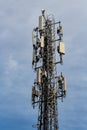 Gray metal cell tower carrying antennas of cellular networks on the blue sky with white clouds background in sunny day. Vertical