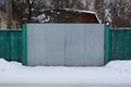 Gray metal gates and wooden green fence in the street in white snow Royalty Free Stock Photo