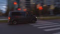 Gray minivan Volkswagen Transporter driving down the street, crossing a pedestrian crosswalk, evening time, motion blur, panning. Royalty Free Stock Photo