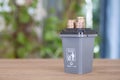 A gray model of trash can with other trash and a pile of dollar coins on its lid