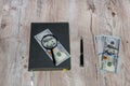 Gray notebook, dollars, magnifier and pen on a wooden table