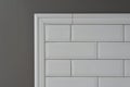 Gray painted wall, part of the wall is covered tiles small white glossy brick, ceramic decorative molding tiles, detail of intrica