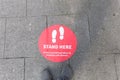 Gray pair of shoes standing front of a red sign saying stand here to avoid spread of covid19. Covid, new normal life concept