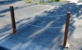 Gray pillars separating the park path from the road. deliberately rusty steel bollards bent into a double space slot connected by