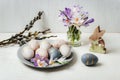 Gray plate with painted Easter eggs and wooden toy bunny, crocus flowers on white table. Easter greeting card Royalty Free Stock Photo