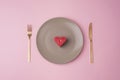 Gray plate with red candle in a shape of heart, fork and knife on pink background. Valentines day concept. Top view