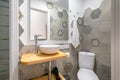 Gray polygonal tiles with an ornament in a compact bathroom with a toilet bowl and a sink. Concept of a stylish designer