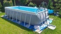 The gray rectangular frame swimming pool stands on a grassy lawn. The water is cleaned with a filter. Next to the metal fence ther Royalty Free Stock Photo