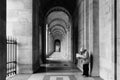 Gray scale shot of a man reading a newspaper in a corridor of arcs of a building in Paris