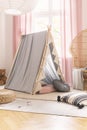 Gray scandi tent in cute little`s girl playroom with wicker peacock chair, pillows and carpets, real photo