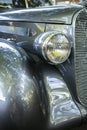 Gray shiny vintage retro car with a hinged round headlight and a large grille displayed at a provincial town street exhibition