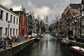 Gray Silhouettes in Amsterdam: Canals, Typical Houses and the Church that Resists the Cloudy Sky.