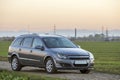 Gray silver empty car parked on gravel rural road on blurred green meadows, distant mountain range and clear sky at sunset copy Royalty Free Stock Photo