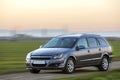 Gray silver new shiny car moving on empty rural road on blurred green meadows and clear foggy sky copy space background. Royalty Free Stock Photo