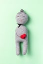 Gray sleeping and smiling handmade doll with red heart in her hands from the threads on mint green background. Vertical photo