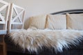 Gray sofa with boucle upholstery fabric and white decorative fluted cushions. White rug or bedspread made of faux fur