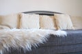 Gray sofa with rough upholstery fabric boucle and white decorative fluted cushions. A long pile white faux fur rug or