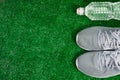 Gray Sports Running Shoes and bottle of water on green grass.