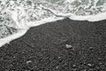 A gray stone heart-shaped lies on the shore with sea foam and clear water on a black sand beach. Concept of love, wedding, freedom Royalty Free Stock Photo