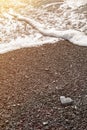 A gray stone heart-shaped on the shore with sea foam and clear water on a black sand beach on sunset. Concept of love, wedding, Royalty Free Stock Photo