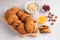 On a gray table are oatmeal cookies, honey, hazelnuts, oatmeal and cranberries in a plate