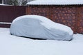 Gray tarp covering on a car in the snow by the brown fence