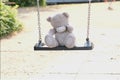 Gray teddy bear sitting alone on swing, concept of loss of parents, loneliness of children, caring for orphans