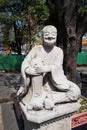 Gray Thai stone monument to a smiling man on a pedestal in a relaxed pose.