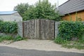 Gray wooden gate and a fence overgrown with fences near the asphalt road Royalty Free Stock Photo