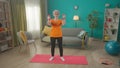 Grayhaired elderly woman doing fitness with dumbbells at home. A mature woman build up biceps, trains triceps, keeps her