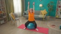 A grayhaired retired woman sitting on a fitness ball performs an exercise with dumbbells. An elderly woman raises