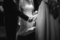 Grayscale closeup of bride and bridegroom holding each other& x27;s hand and standing in front of priest